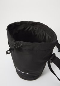 Black fabric bucket bag with a drawstring closure, smooth texture, and adjustable strap. Logo printed on the front.