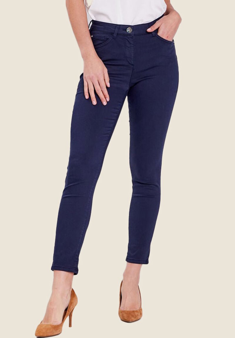 Jeans skinny blu navy con una texture liscia, dotati di chiusura con bottone, tasche frontali e una vestibilità affusolata, abbinati a tacchi color cammello.