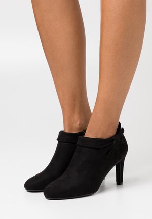 Botines de ante negros con un dobladillo y un detalle de lazo en la parte posterior, con punta afilada y un tacón alto delgado.