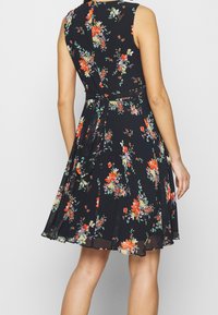 Robe noire à fleurs avec un corsage ajusté et une jupe évasée. Elle présente des motifs floraux colorés, un design sans manches et un détail de taille nouée.
