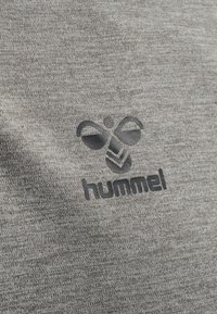 Tissu gris avec une texture chinée, présentant un logo foncé avec des formes abstraites et le mot "hummel" en dessous.
