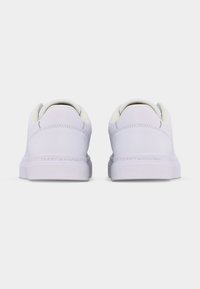 Ζευγάρι λευκά παπούτσια χαμηλού τύπου, φαίνονται από πίσω, με την επιγραφή "Tommy Hilfiger" ανάγλυφη στη φτέρνα της σόλας.