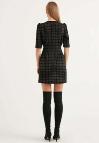 Schwarz-weißer kariertes Kleid mit kurzen Puffärmeln, taillierter Silhouette und geradem Saum. Kombiniert mit schwarzen Stiefeln über dem Knie.