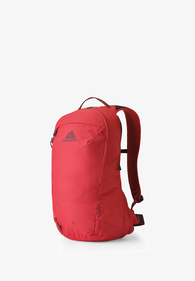 Sac à dos rouge avec une surface lisse, des bretelles rembourrées et une poignée supérieure. Il comprend un compartiment principal zippé et une poche avant.