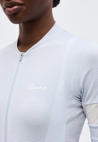 Κοντινό πλάνο ενός ατόμου που φοράει ελαφριά γαλάζια, υφασμάτινη φανέλα ποδηλασίας με φερμουάρ μπροστά και το λογότυπο «Rapha» στο στήθος.