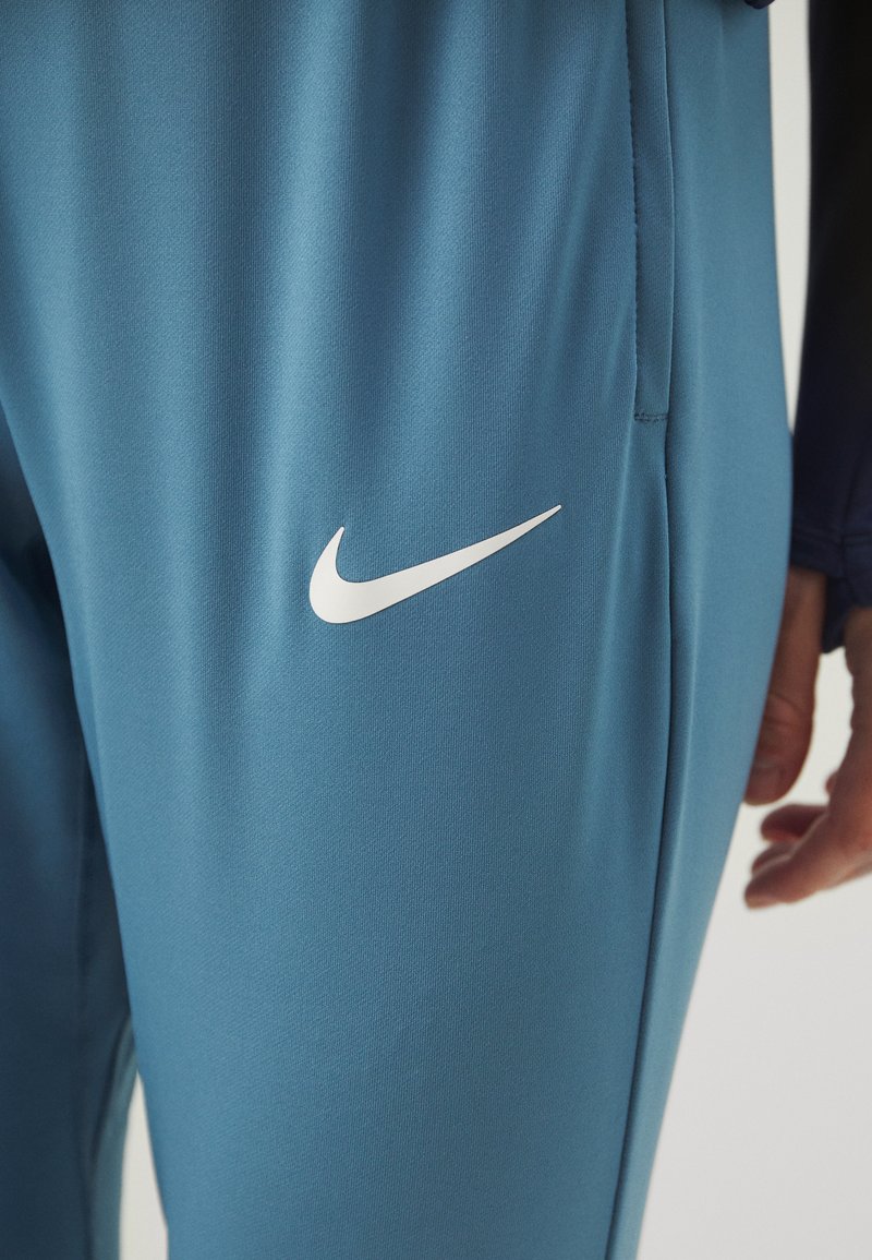 Blaue Sporthosen aus glattem, leichtem Stoff mit dem weißen Nike-Swoosh-Logo. Sie haben eine taillierte Passform und seitliche Taschen.