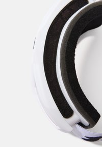 Fones de ouvido brancos com almofadas de espuma preta e suave, apresentando uma casca externa lisa e uma faixa de ajuste em tecido estampado.
