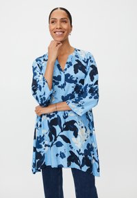 Niebieska tunikowa bluzka w kwiaty o luźnym kroju, z dekoltem w serek, rękawami do łokcia oraz jasnoniebieskimi i ciemnoniebieskimi wzorami kwiatowymi.