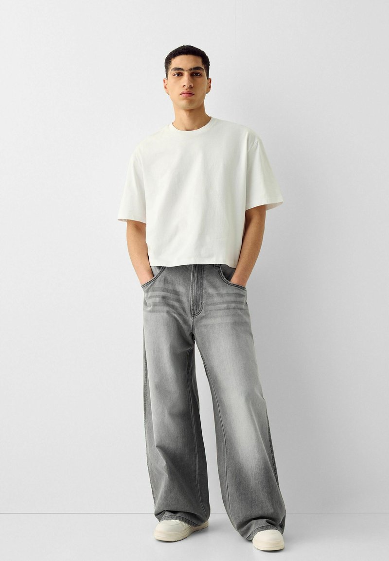 T-shirt bianco cropped abbinato a jeans in denim grigio a taglio largo. I jeans hanno una finitura scolorita e dettagli di cucitura sottili. Sneakers di tonalità chiara.