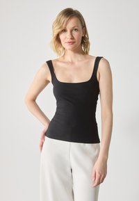 Top sin mangas negro acanalado con escote cuadrado y tirantes anchos, diseño ajustado, combinado con pantalones blancos de pierna ancha.