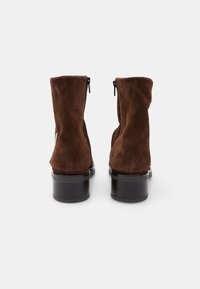 Stivali ankle in suede marrone con un design leggermente morbido. Caratterizzati da un tacco a blocco nero e cerniere laterali per una facile vestibilità.