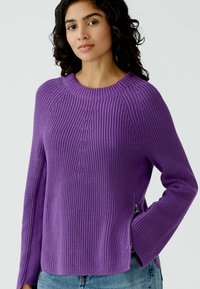 Lila gestrickter Pullover mit strukturiertem Rippmuster, rundem Ausschnitt und seitlichen Reißverschlüssen. Lange Ärmel mit lockerer Passform und lässigem Design.