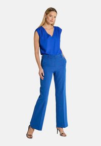 Blauwe mouwloze blouse met een V-hals, gecombineerd met hoge blauwe broeken met een rechte pijp en subtiele voorplooien.