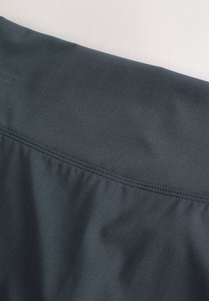 Tamsiai pilka audinys su lygiu paviršiumi ir šiek tiek tampri. Viršutinėje krašte yra subtilus rauktas siūlė, suteikianti prigludusį dizainą.