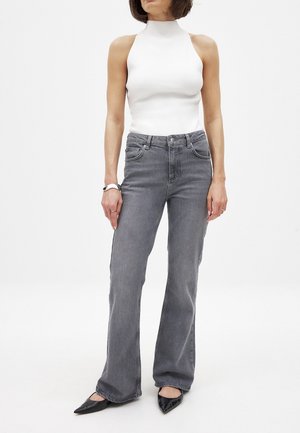 Grå denim flared jeans med forlommer og subtilt slid, parret med en tætsiddende hvid højhalset top og sorte spidse flade sko.
