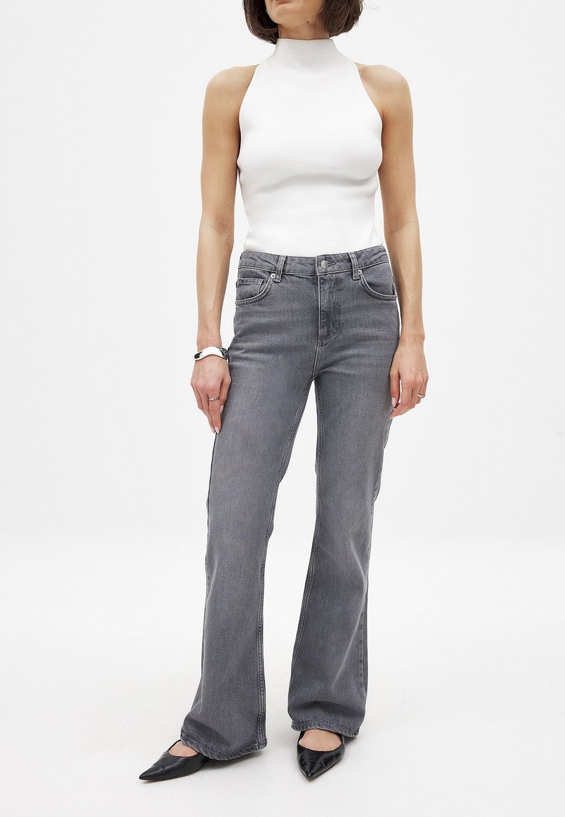 Harmaat farkkujen leveälahkeiset housut, joissa on etutaskut ja hienovarainen kulutus, yhdistettynä muotonsa mukaiseen valkoiseen korkea-kaulaiseen paitaan ja mustiin kärkitossuihin.