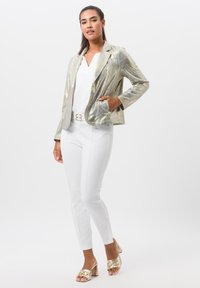 Metalen gouden blazer met een gestructureerd ontwerp, gecombineerd met een witte top en slanke witte broek. Gouden blokhak sandaal met een accent gesp.