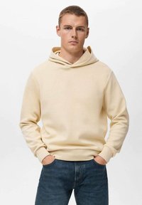 Cremefarvet hættetrøje i blødt stof, med snørredragt og ribbede manchetter. Båret med mørkeblå denimjeans.