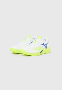 Ζευγάρι λευκά αθλητικά παπούτσια με φλούο κίτρινες σόλες και λεπτομέρειες, με μπλε λογότυπο της μάρκας και λευκά κορδόνια, παρουσιασμένα σε απλό φόντο.