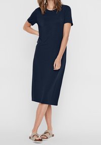 Mörkblå, kortärmad klänning i knälängd gjord av mjukt tyg med en avslappnad passform. I kombination med lätta sandaler med platta sulor och rosettaccenter.