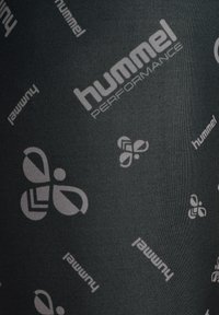 Svart tyg med upprepade mönster av ljusgrå Hummel-logotyper och "hummel"-text i olika orienteringar.