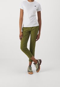 Bílý tričko s kulatým výstřihem a černým logem, olivově zelené zúžené kalhoty a vícebarevné chunky tenisky s texturovanou podrážkou.