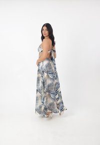Robe maxi avec un motif de feuilles bleu et beige, bretelles fines, dos nu et jupe fluide. Tissu lisse avec une texture soyeuse.