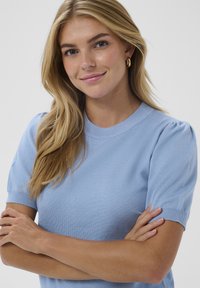 Haut en maille bleu clair à manches courtes avec un col rond et une texture subtilement côtelée. Caractérisé par des manches bouffantes et une silhouette ajustée.