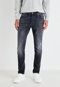 Jeans slim-fit de culoare gri închis, cu un finisaj estompat, având un design cu cinci buzunare, închidere cu buton metalic și bucle pentru curea, asortați cu adidași albi.