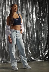 Crop top in navy, wide-leg light blue jeans, and white sneakers. Layers with a light striped shirt. Silver reflective background.