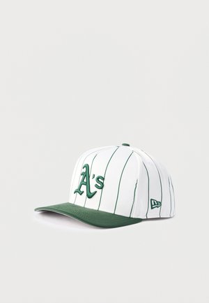 Fehér baseball sapka zöld csíkokkal, zöld karimával és zöld "A's" logóval hímzve az elején, világos háttéren bemutatva.
