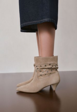 Beige suède enkellaarsjes met een slouchy bovenkant en metalen oogjes, gedragen met donkere cropped spijkerbroeken.
