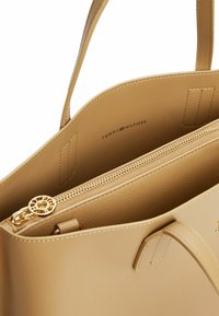 Borsa tote in pelle tan con doppio manico superiore, dotata di una tasca interna con zip e hardware in tono oro. Logo del marchio impresso all'interno.