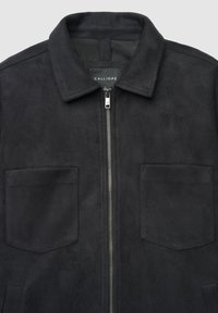 Veste en daim noir avec une fermeture éclair, un col pointu et deux poches plaquées à l'avant. Texture lisse sans motifs visibles ni détails métalliques.
