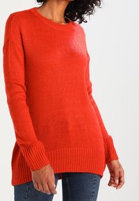 Červený pletený svetr s kulatým výstřihem, žebrovaným lemem a manžetami a volným střihem, s texturovanou látkou a dlouhým střihem.