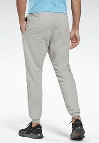 Sudadera gris con diseño de pierna ajustada, puños elásticos y bolsillos laterales, combinada con zapatillas deportivas negras. Vista trasera mostrada.