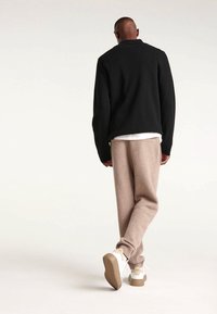 Schwarze Strickjacke, beigefarbene lässige Hose, weiße Sneakers mit braunen Akzenten. Sanfte Texturen, minimalistisches Design und neutrale Farbpalette.