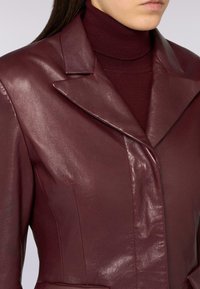 Blazer in pelle borgogna con finitura lucida, colletto appuntito e vestibilità sartoriale, indossato sopra un dolcevita abbinato.