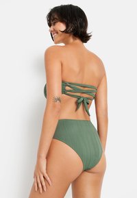 Žalias bikinis, turintis bepečių viršų su susukti akcentais nugaroje ir aukštai juosmeniui priglundančias kelnaites su vertikaliu ruoželiu.