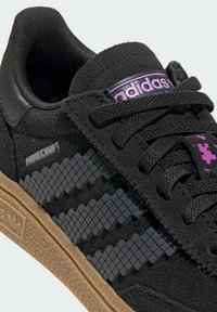 Sneaker in suede nero con logo viola, caratterizzata da dettagli pixelati neri, lacci piatti e suola in gomma color miele con battistrada testurizzato.