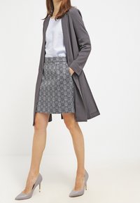 Abrigo largo gris sobre una blusa azul claro combinada con una falda estampada; unos tacones altos gris claro realzan el conjunto. Texturas de tela suaves visibles.