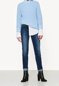 Light blue knitted sweater with dropped shoulders, layered over a white button-up shirt. Worn with dark blue skinny jeans and black heeled boots.
