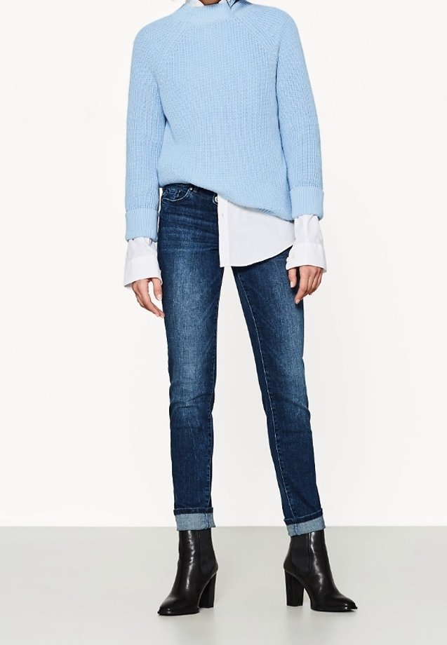 Light blue knitted sweater with dropped shoulders, layered over a white button-up shirt. Worn with dark blue skinny jeans and black heeled boots.