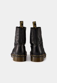Zwarte leren enkelboots met een gestructureerde afwerking, gele stiksels langs de zool en trekflappen met het label "WITH SOL ES" aan de achterkant.