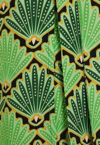 Tissu vert avec un motif audacieux et répétitif de feuilles en forme d'éventail en vert foncé et noir, rehaussé de détails jaunes et blancs.