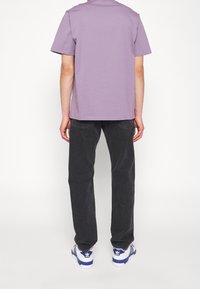 Camiseta de algodón lavanda, corte holgado, combinada con pantalones de mezclilla oscuros y zapatillas azul y blancas con un logo en el lateral.