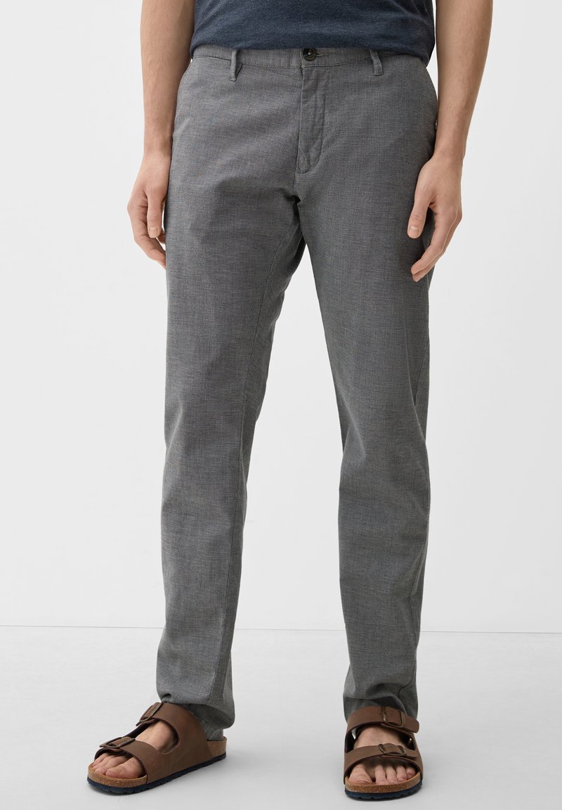 Grå mönstrade byxor med rak passform, tillverkade av lätt material. Med en främre knäppning och sidofickor, kombineras med bruna sandaler.