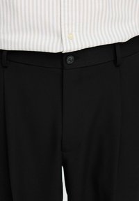 Nära bild av svarta byxor som är knäppta med en knapp, i kombination med en beige och vit randig skjorta som är instoppad.