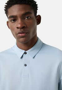 Lichtblauw poloshirt gemaakt van een gestructureerde stof met een omgeslagen kraag, een knoopsluiting met drie knopen en een subtiel logo op de borst.