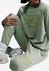 Completo sportivo Nike verde, composto da una felpa con colletto a girocollo e pantaloni affusolati, con logo ricamato in oro e calzini bianchi alla caviglia.